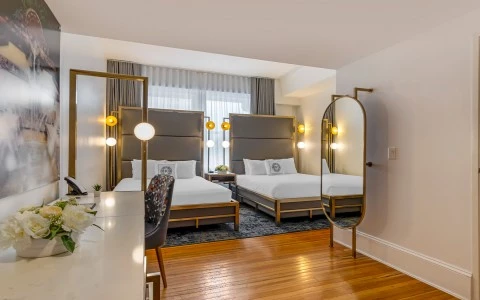 A hotel room with two beds, two mirrors, a desk, and flowers.