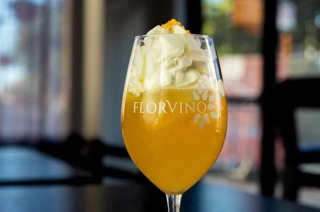 a glass of orange liquid with whipped cream