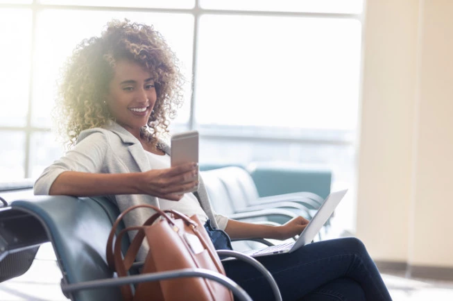 A woman sits in a lobby area with a laptop and cell phone.