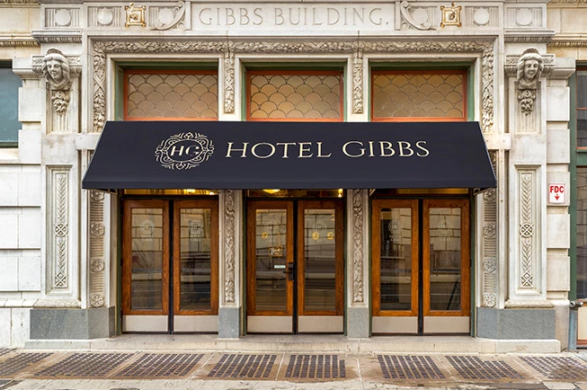 The exterior of a building with a black awning reading 'Hotel Gibbs'