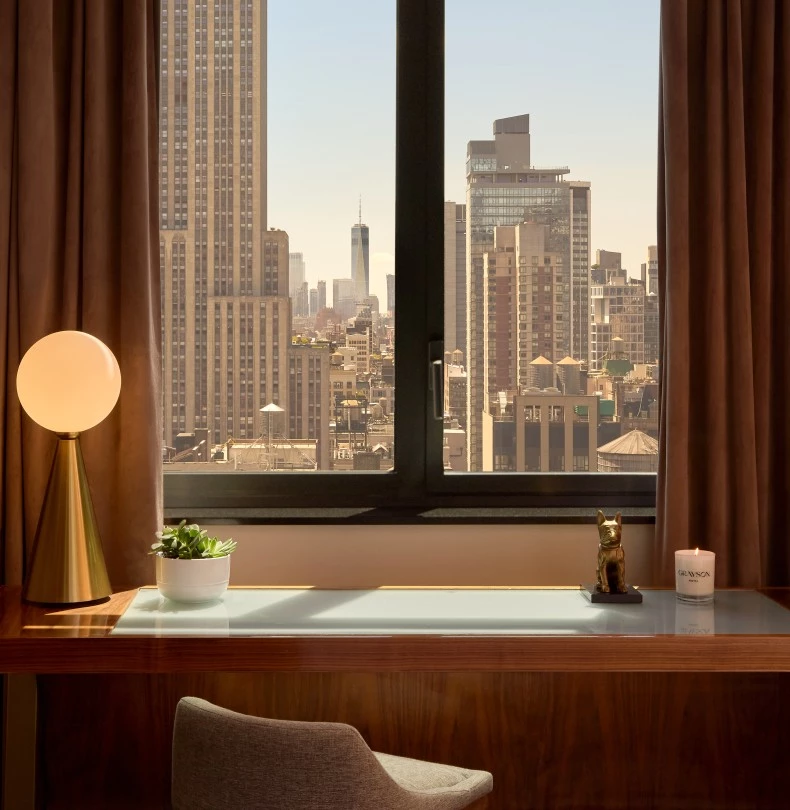 a desk with a lamp and a window with a city view 