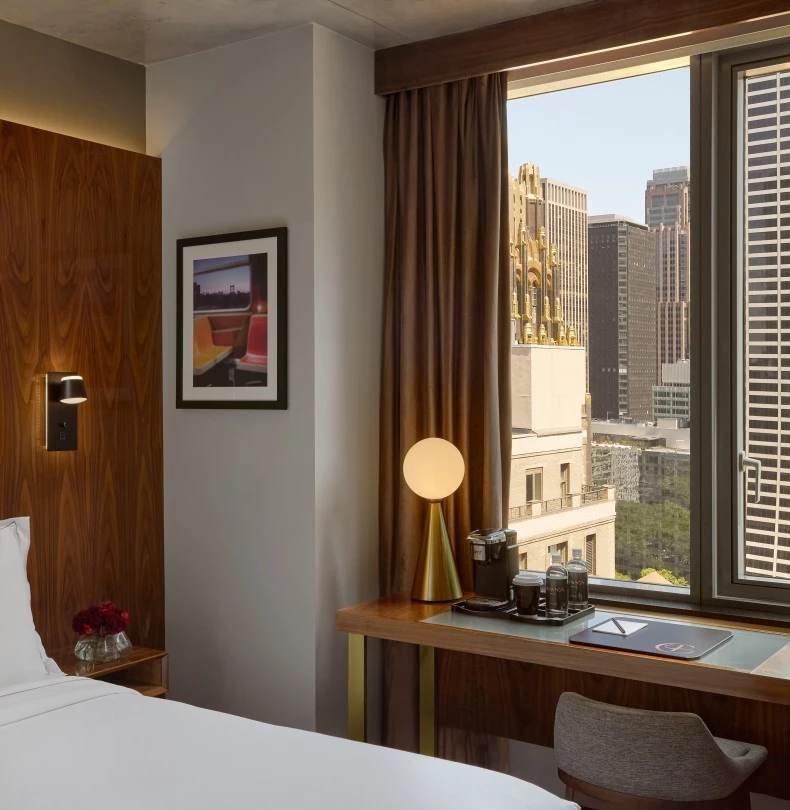 a room with a bed and a desk and a window with a city view 