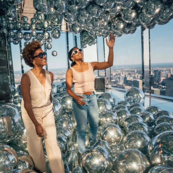two women standing in front of a large pile of silver balls