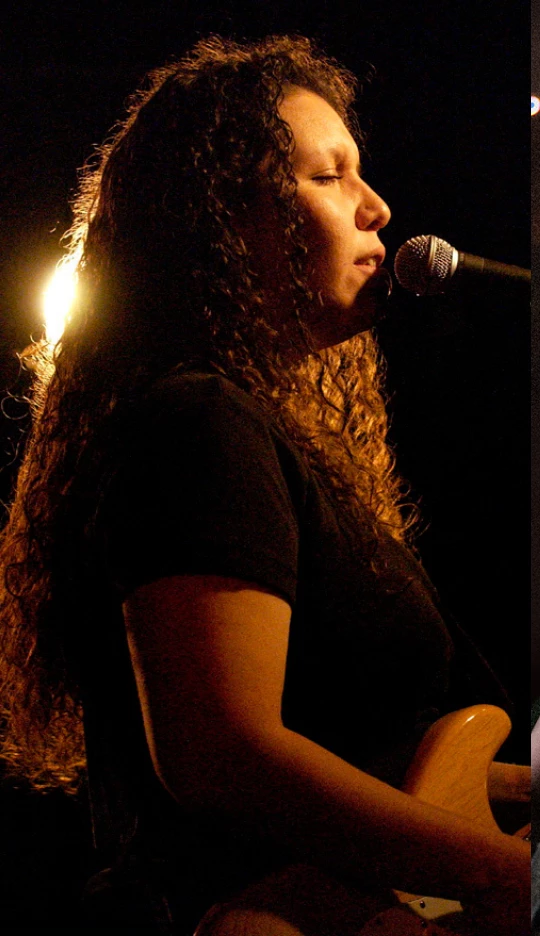 a woman with long curly hair singing into a microphone