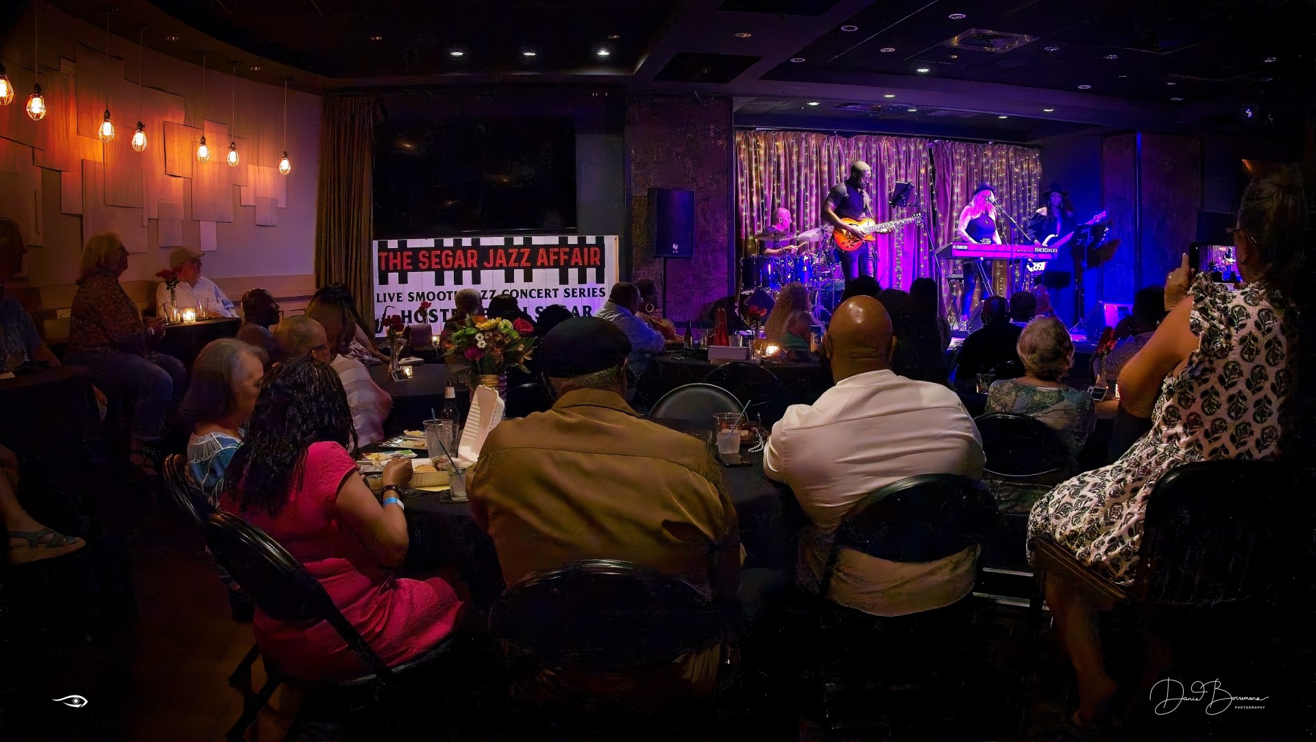a group of people sitting at tables and a stage with a man playing a guitar