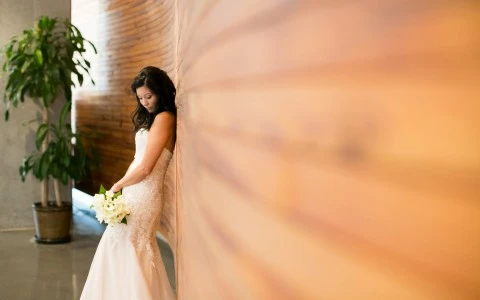 bride leaning up against the wall looking down at her bouquet
