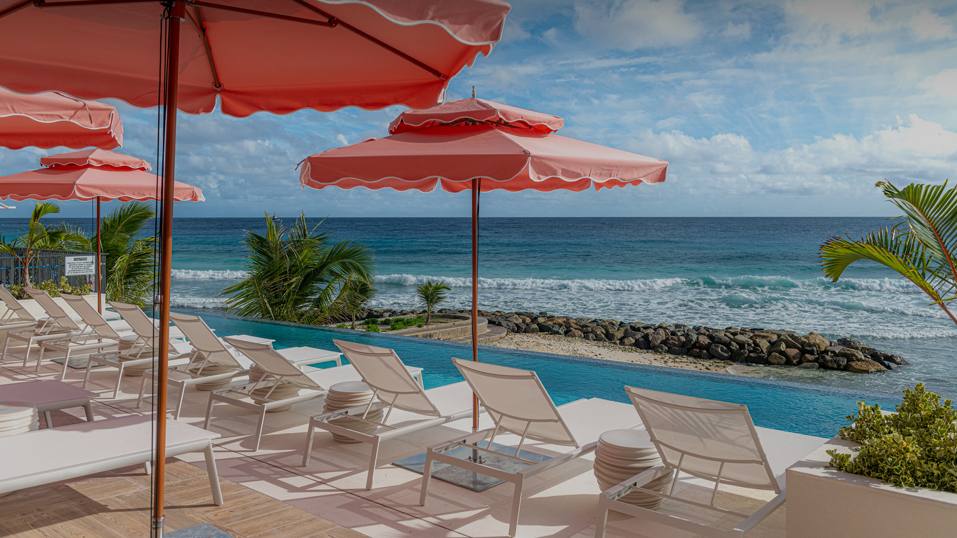 a pool with chairs and umbrellas by the ocean