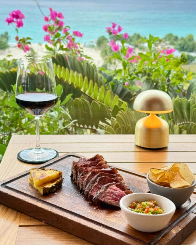 a steak and chips on a wooden board with a glass of wine