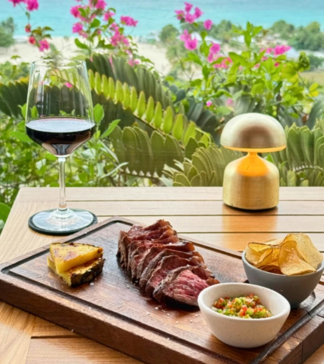 a steak and chips on a wooden board with a glass of wine