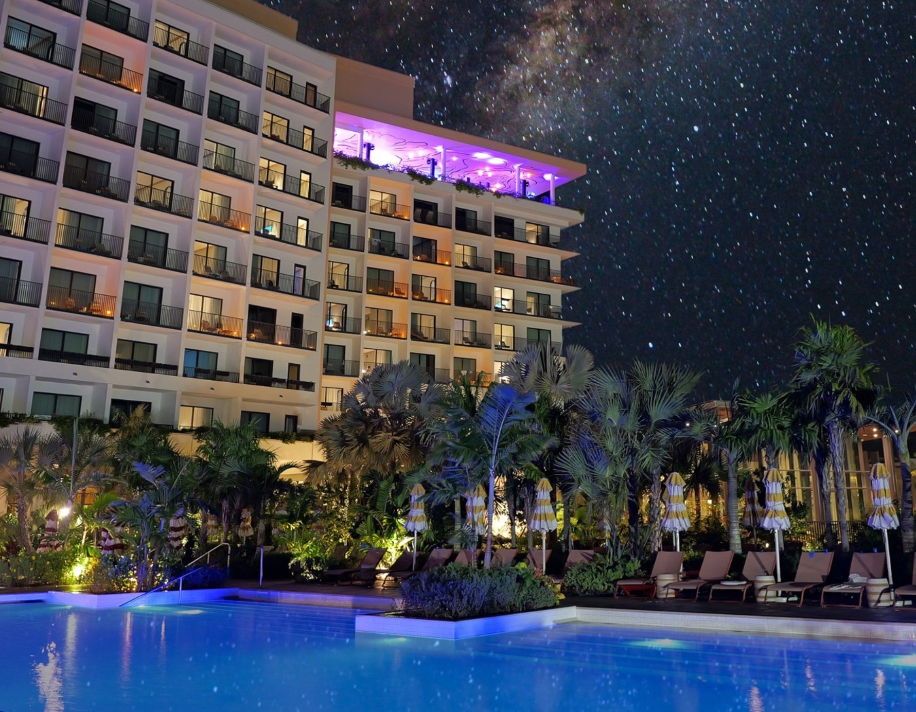 a pool with palm trees and a building with stars in the sky