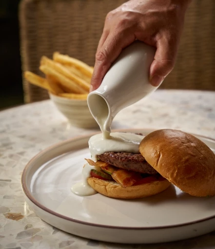 a person pouring milk onto a burger