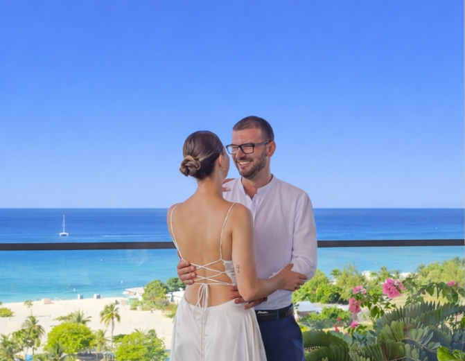a man and woman standing on a balcony with a beach and water in the background