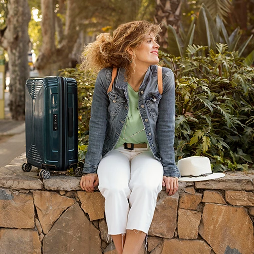 a woman sitting on a stone ledge with a suitcase