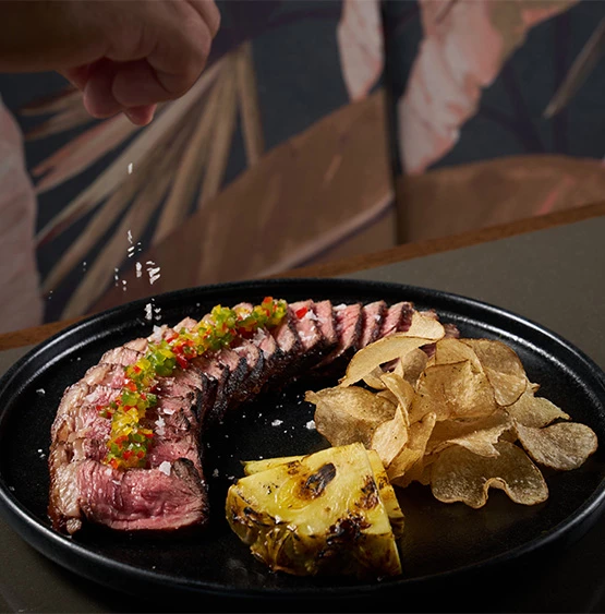a plate of food with a hand sprinkling salt