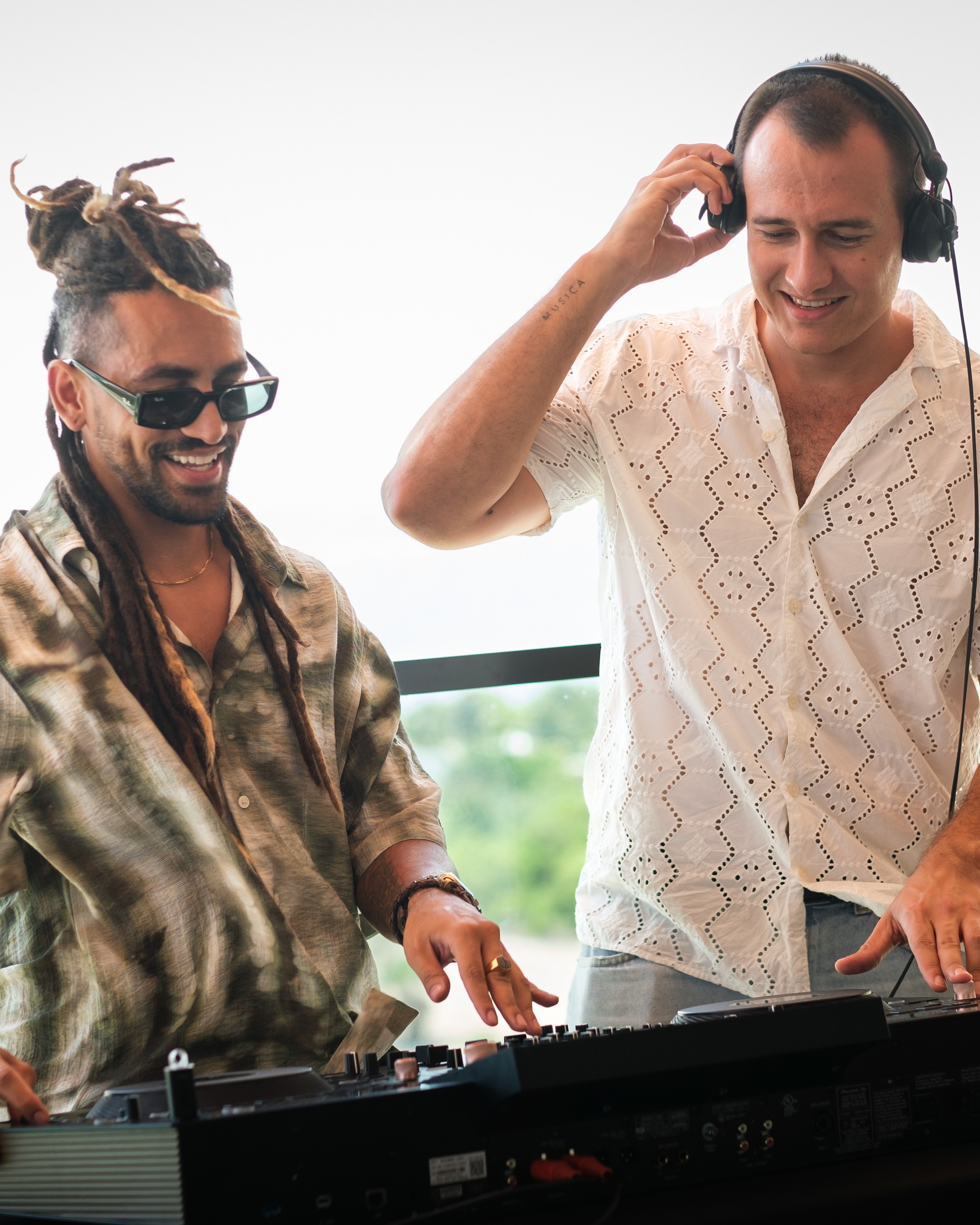 two men wearing headphones and standing next to a keyboard