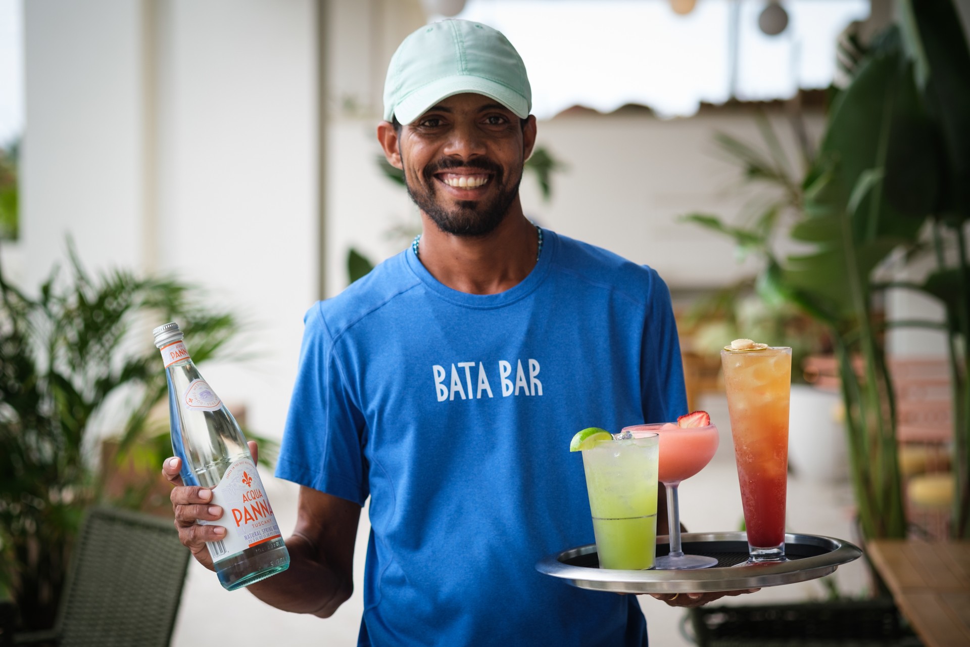 a man holding a tray of drinks and a bottle