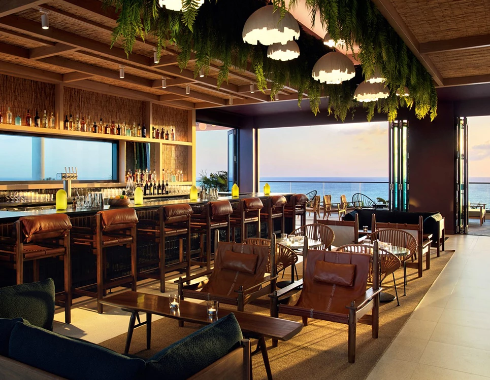 a room with a bar and chairs over looking water