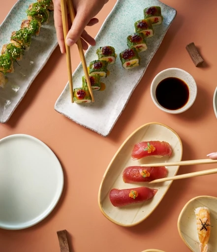 a person holding chopsticks to a plate of sushi