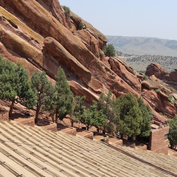 a red rock mountain with trees with Red Rocks Amphitheatre in the background