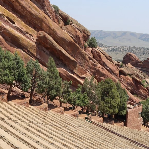 a red rock mountain with trees with Red Rocks Amphitheatre in the background