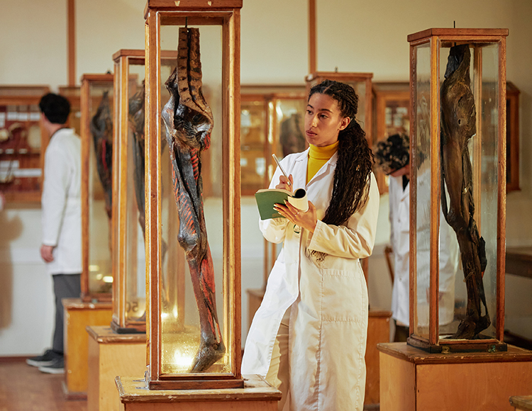 a woman in a white coat standing in front of a glass case with a notepad