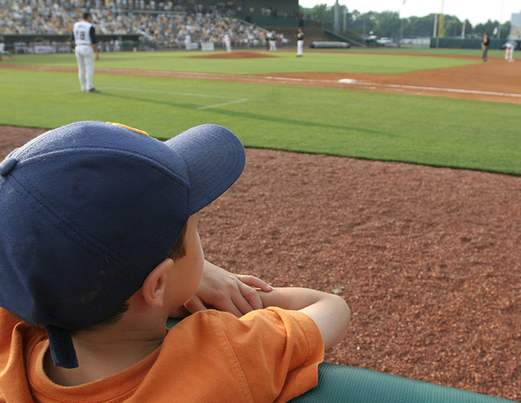 a boy in a baseball cap watching a baseball game