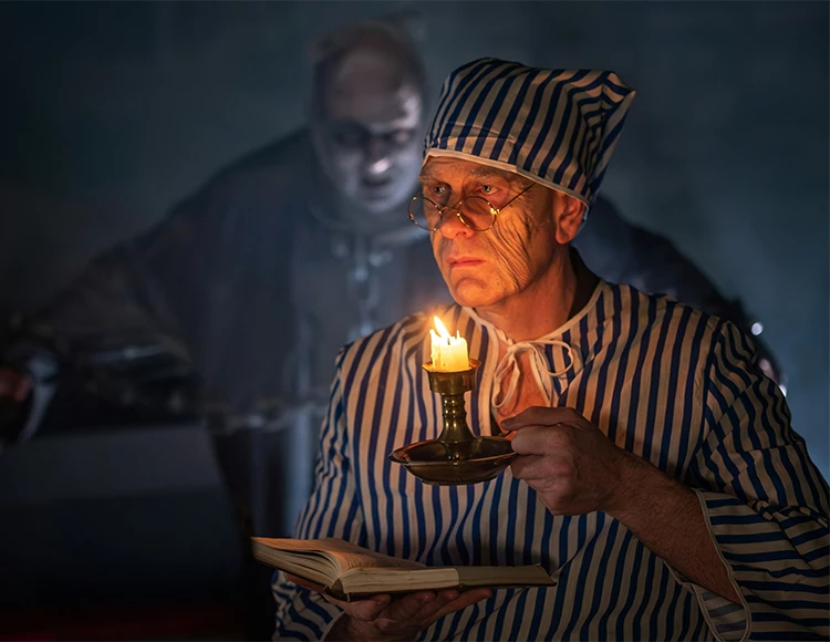 a man in striped pajamas holding a candle and a book