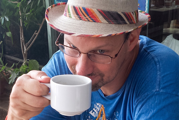 a man wearing a hat and drinking from a white mug