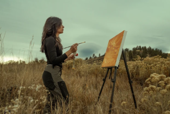 a woman painting on a canvas in a field