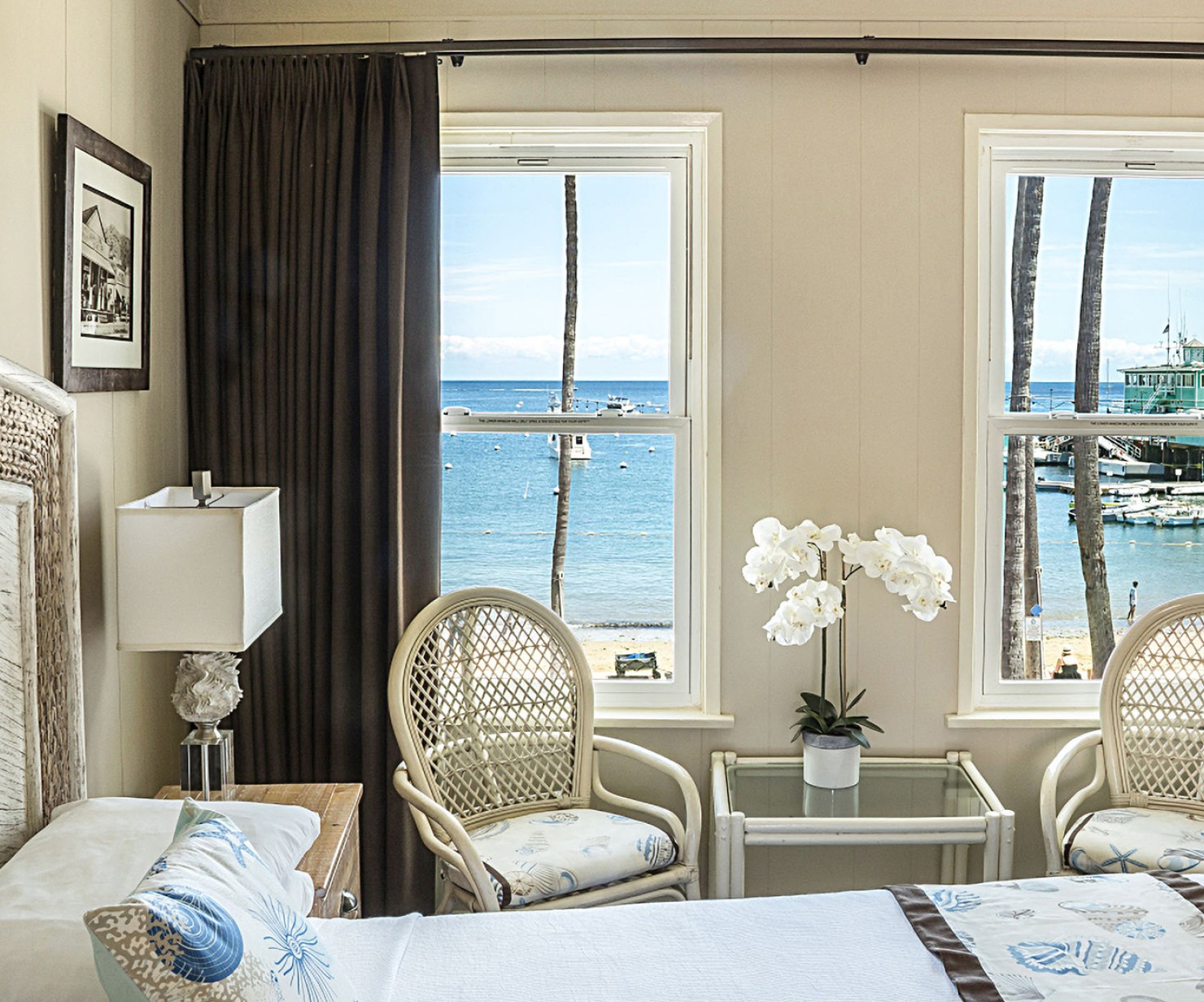 a room with a bed and chairs and a table with a lamp and a window with a view of the ocean