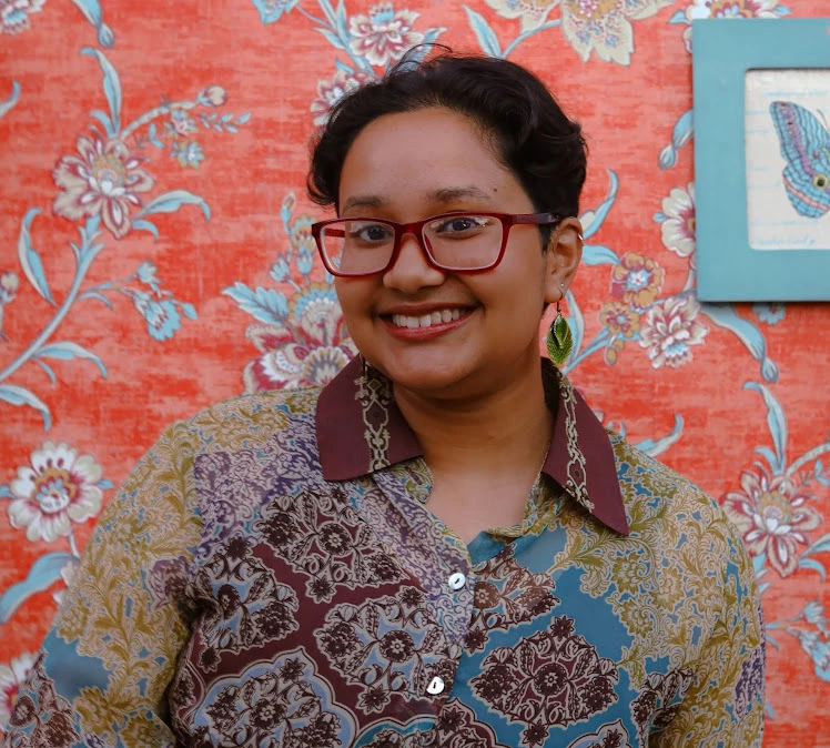 a woman smiling in front of a floral wallpaper