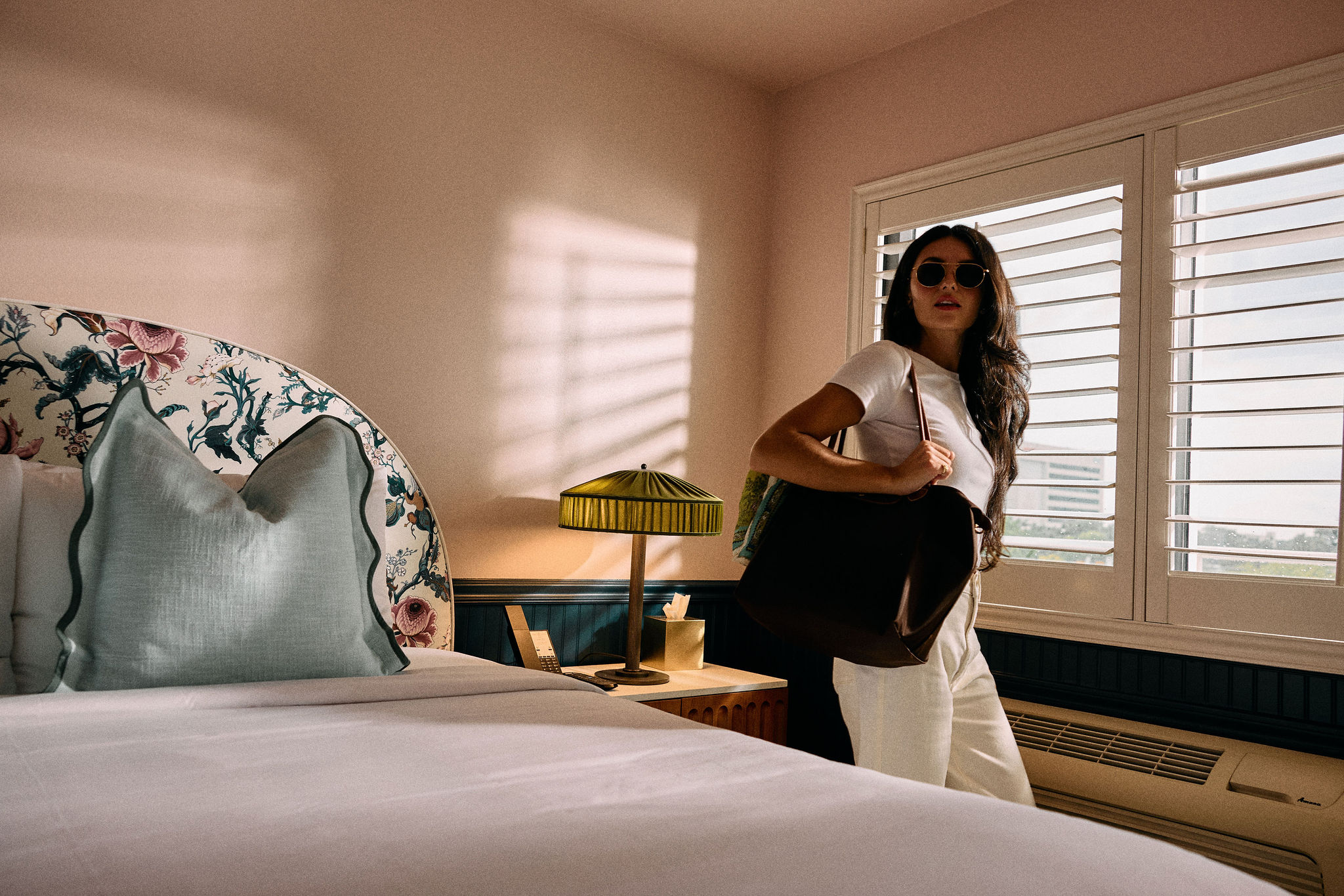 a woman in a room with a bed and a lamp