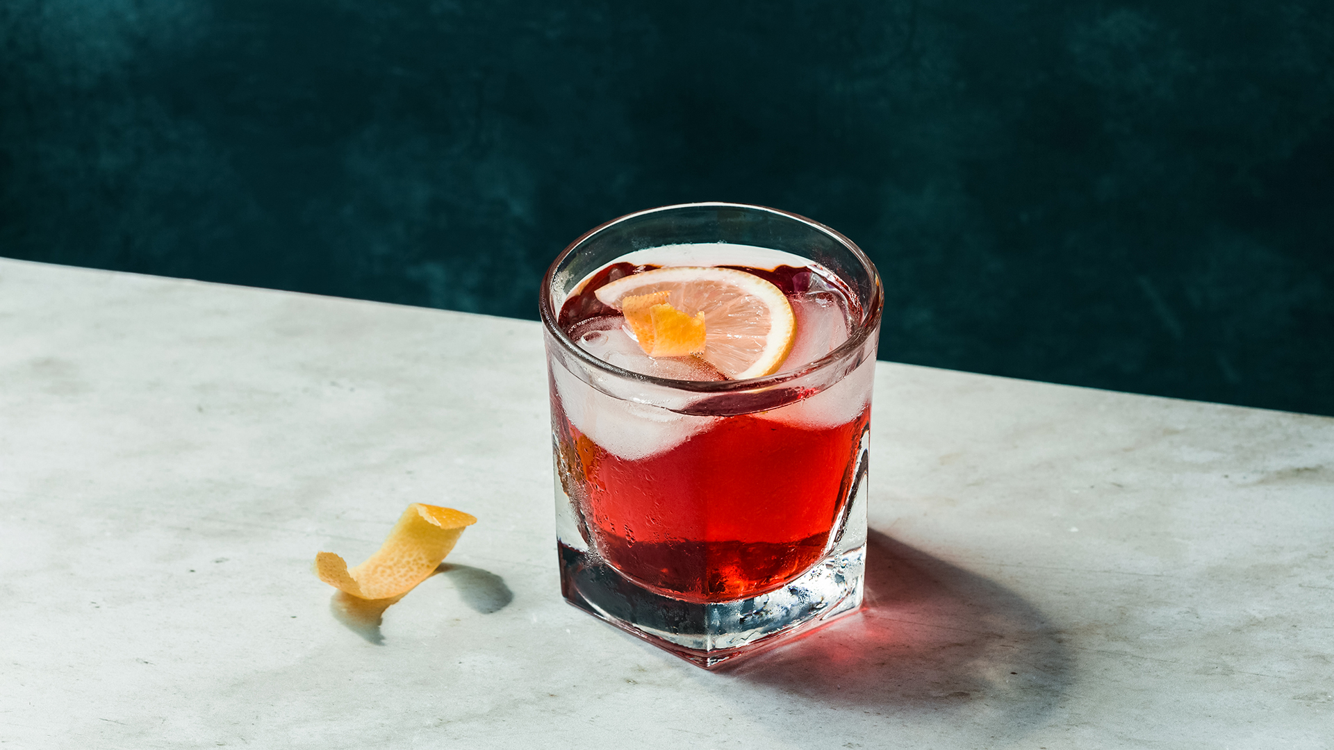 a glass of red liquid with a lemon slice and ice