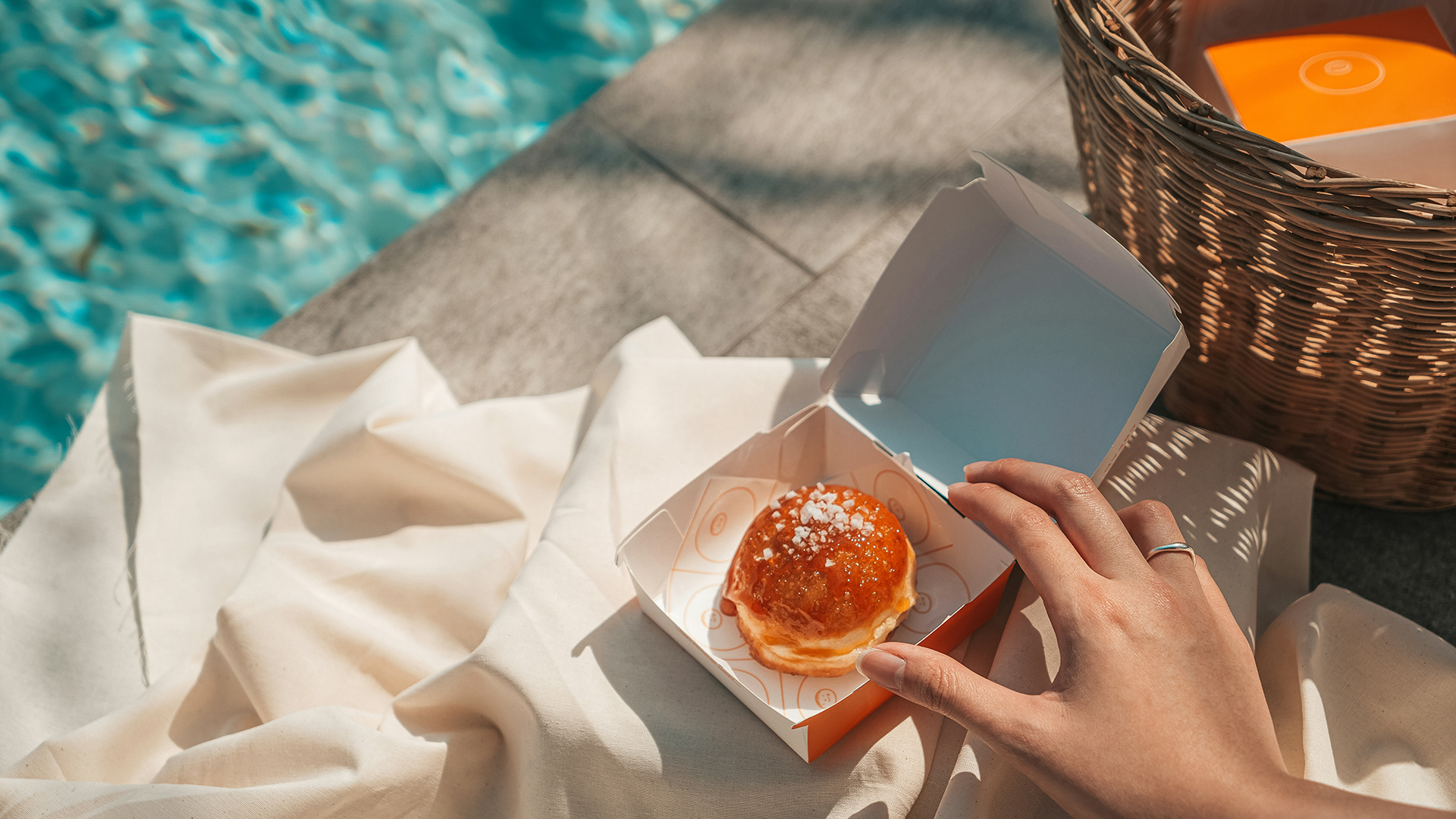 a hand holding a small pastry in a box next to a pool secondary slider