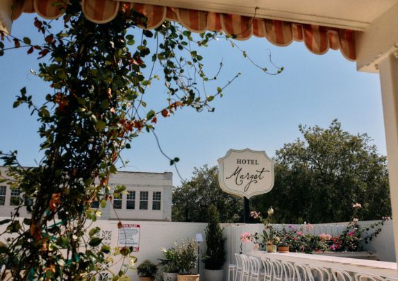 a sign with a white wall and chairs and a tree
