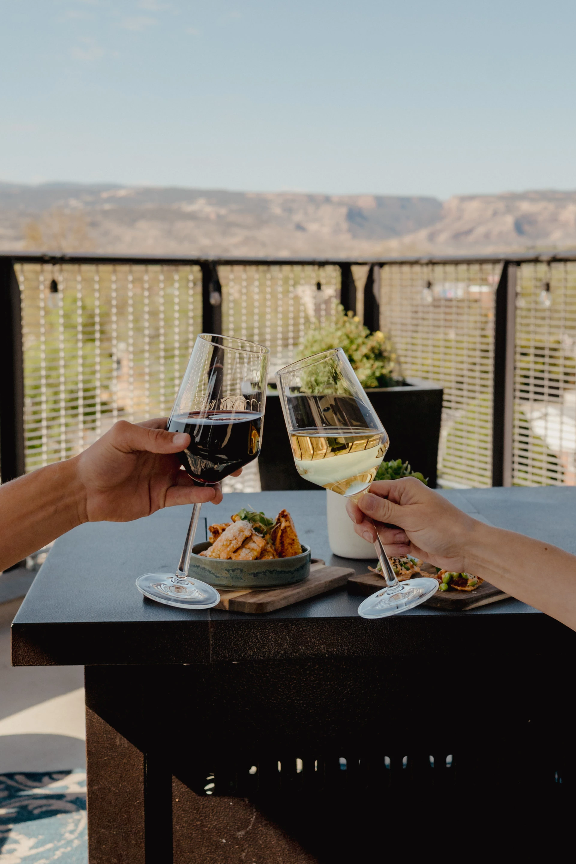 a pair of hands holding wine glasses with food on a table
