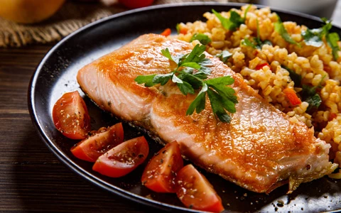 A plated dish of salmon, tomatoes, and grains.