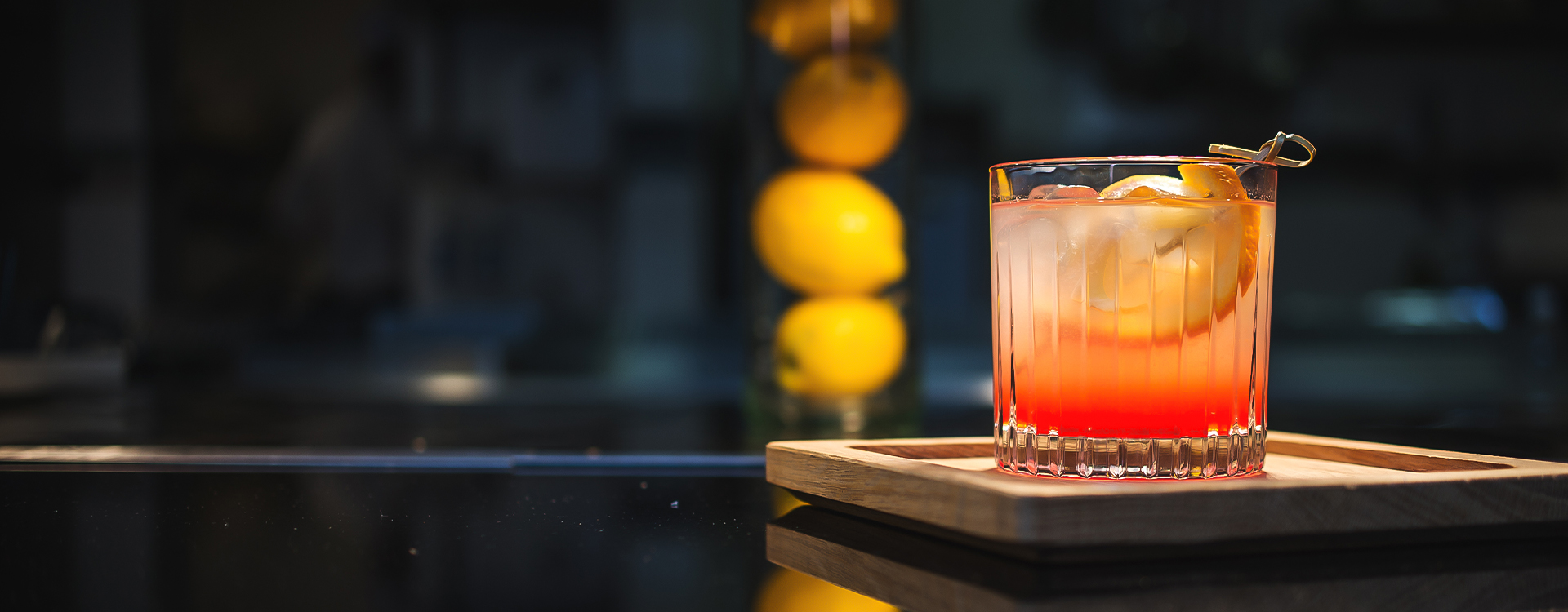 a glass of red and orange liquid on a wooden tray