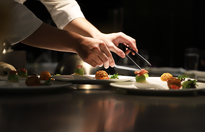 a person holding tongs to a plate of food