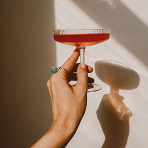 Woman hand with a ring on a finger holding a red cocktail and a shadow of it