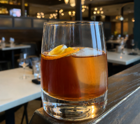 a glass of brown liquid with ice and orange slice