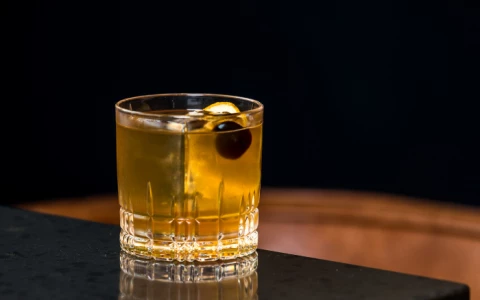 a glass of liquid with a olive on a black surface