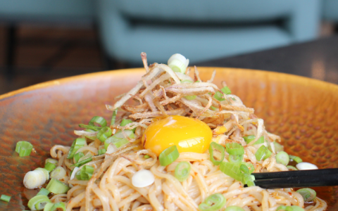 a bowl of noodles with a yolk and green onions