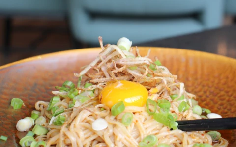 a bowl of noodles with a yolk and green onions