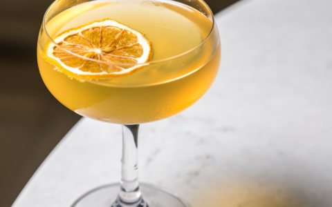 a glass of yellow liquid with a slice of lemon on top of it