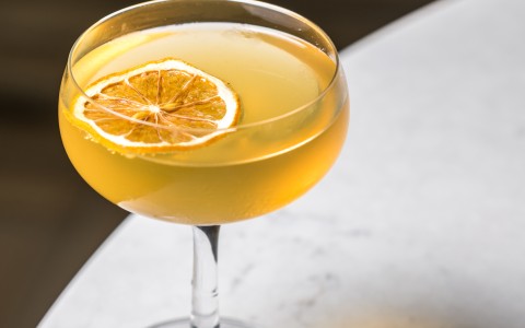 a glass of yellow liquid with a slice of lemon on top of it