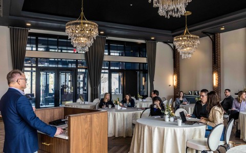 a man speaking at a podium in a room with tables and chandeliers
