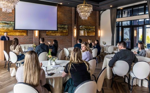a group of people sitting at tables in a room with a projector screen