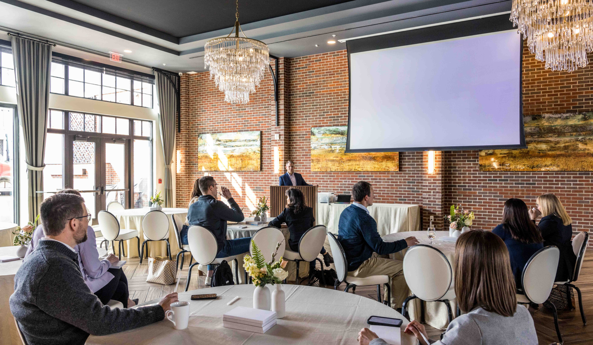 a group of people sitting around tables and a projector screen