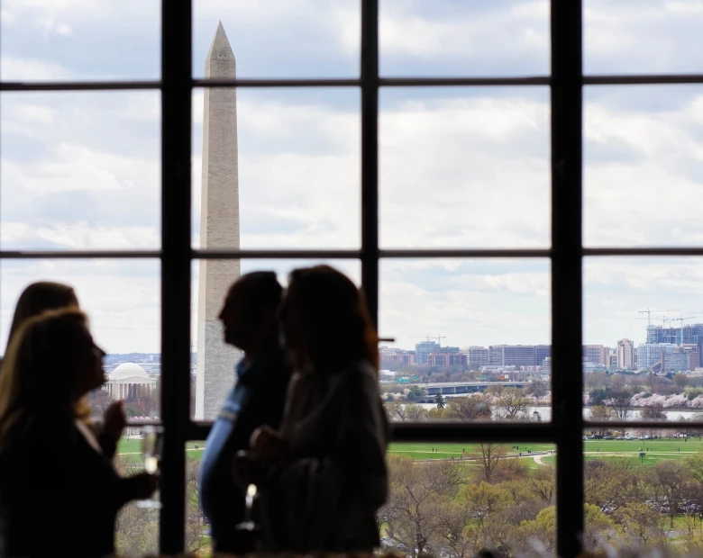 a group of people standing in front of a window overlooking at a monument